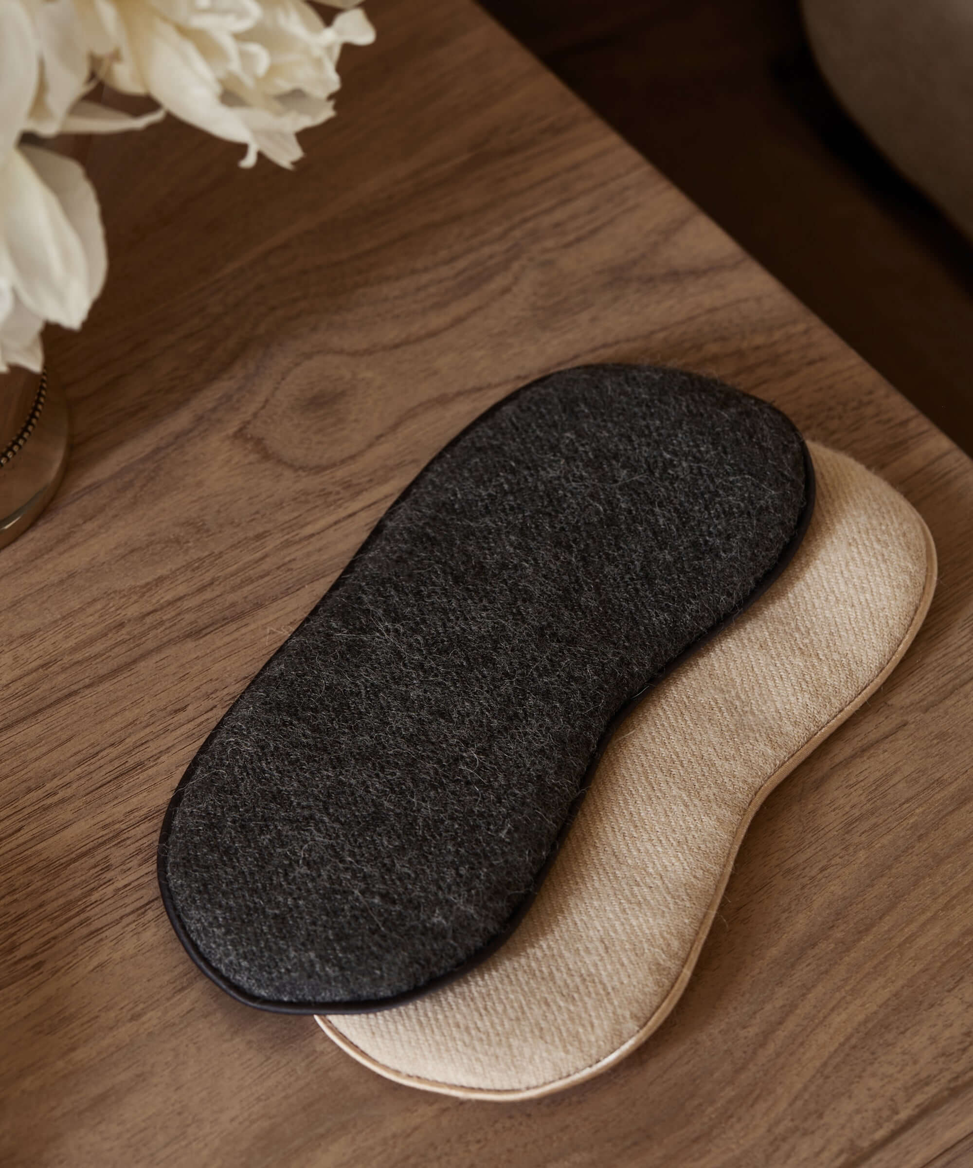Two lounge sleep eye masks resting on a wooden table, one black and one beige, ideal for relaxation.