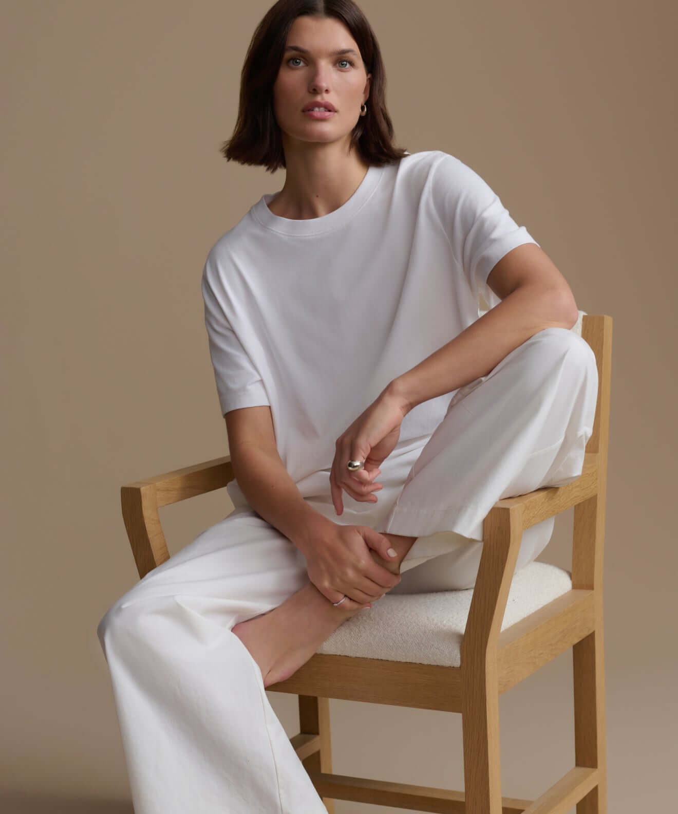 Model wearing a simple white top from the Tops collection, sitting on a chair with a neutral background.